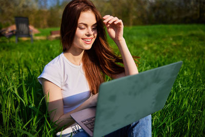 Portrait of young woman using laptop on field