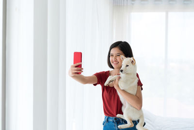 Cheerful woman holding dog taking selfie at home