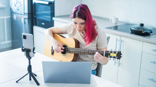 Young woman using mobile phone while sitting on laptop