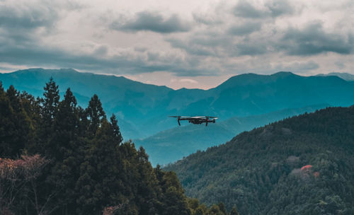 Low angle view of drone flying over mountains against sky