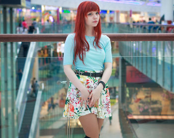 Beautiful woman with redhead looking away while standing by railing at shopping mall
