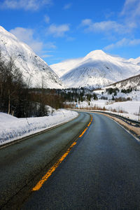 Road by snowcapped mountains against sky