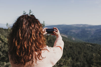 Rear view of woman photographing mountains through smart phone