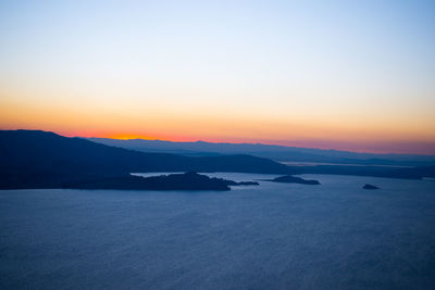 Scenic view of sea by silhouette mountains against clear sky