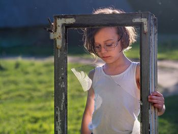 Portrait of girl standing on wooden post at field