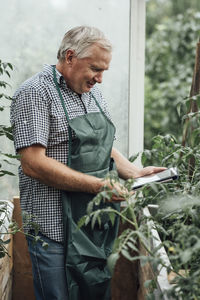 Mature man, gardener in greenhouse using digital tablet