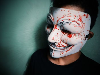 Close-up of young man wearing mask standing against wall during halloween