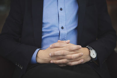 Midsection of businessman sitting with hands clasped at airport