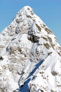 Low angle view of snowcapped mountain against clear blue sky