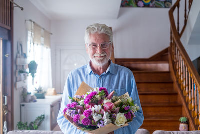 Portrait of smiling man holding bouquet standing against wall