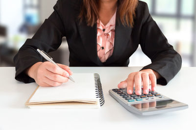 Midsection o businesswoman writing on book in office