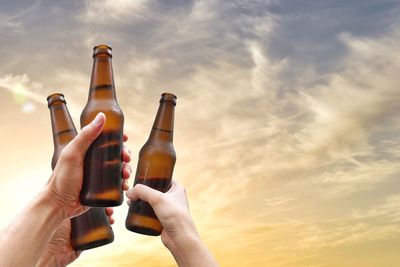 Midsection of woman holding glass bottle against sky