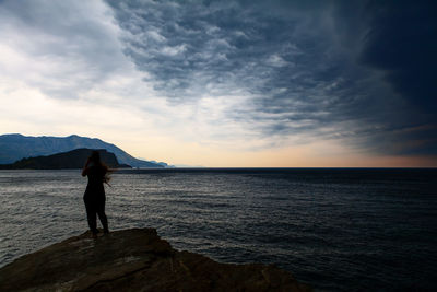 Silhouette man standing in sea against sky during sunset