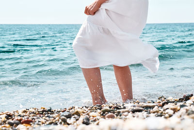 Happy woman in white dress walks in the pebble beach with crystal sea and blue sky. 