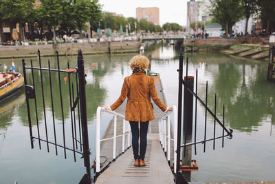 Rear view of woman standing on footpath leading towards pier at river