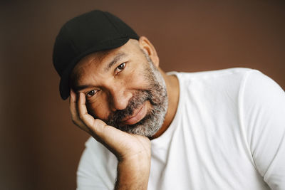 Mature man with hand on chin against brown background