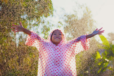 Woman with arms outstretched standing against plants