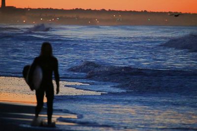 Rear view of silhouette man standing at beach during sunset