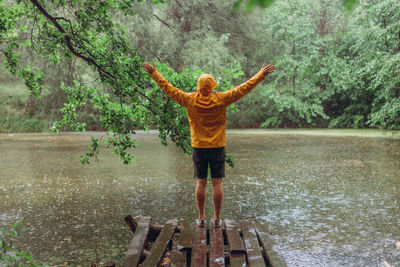 Rear view of person standing by tree in lake