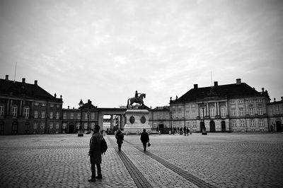 People standing at town square by amalienborg palace against cloudy sky