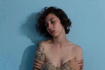Close-up of shirtless woman covering breasts against blue background