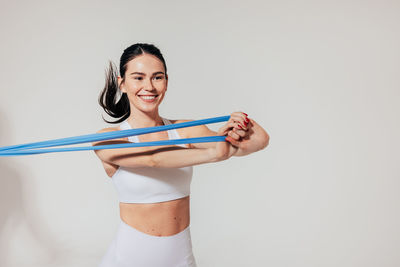 Portrait of smiling young woman holding tape measure against white background