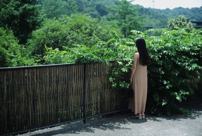 Woman standing by fence against forest