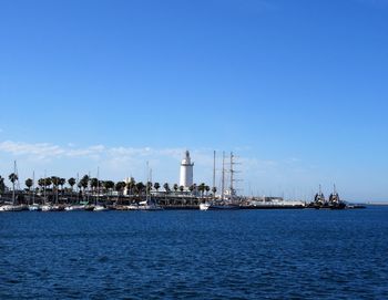 Lighthouse by sea against clear blue sky