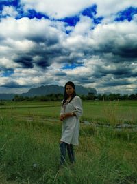 Portrait of mid adult woman standing on grassy field against cloudy sky