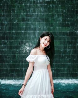 Portrait of smiling young woman standing against waterfall