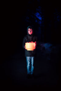 Portrait of teenage girl standing against black background