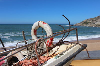 Boat moored on shore at beach against clear blue sky