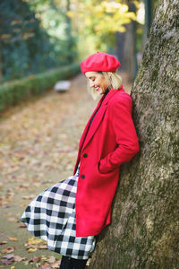 Young woman standing against tree trunk