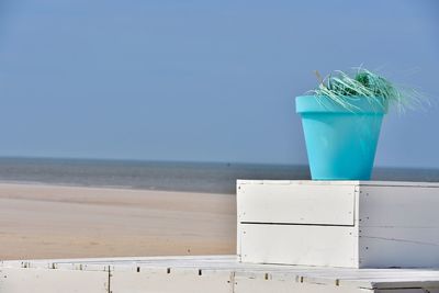 Glass of blue water on beach against sky