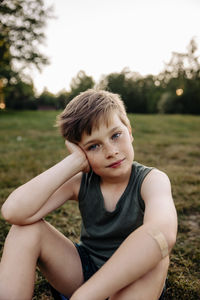 Portrait of boy leaning on elbow while sitting on grass in playground