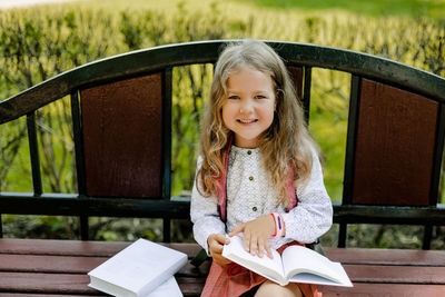 Portrait of a pretty schoolgirl girl sitting with books on a bench in the park or near the school