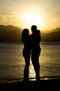 Silhouette romantic couple standing at beach during sunset