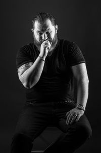 Portrait of young man sitting against black background