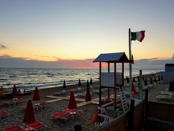 Deck chairs on beach against sky during sunset