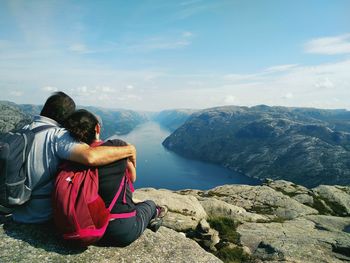 Rear view of couple sitting on mountain against sky