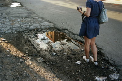 Low section of woman holding camera while standing by puddle on street