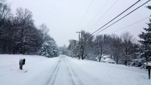 Snow covered road by trees against sky