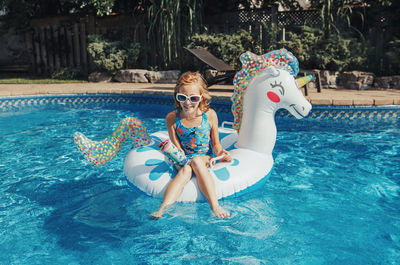 Girl in sunglasses with drink lying on inflatable ring unicorn. summer outdoor water activity 