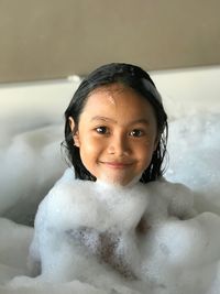 Portrait of smiling girl taking bubble bath in bathroom
