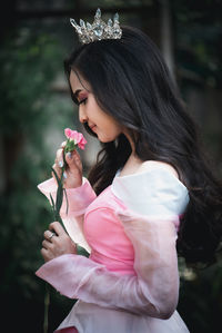 Close-up of smiling woman wearing crown smelling flower standing outdoors