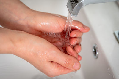 Cropped image of hand touching water from faucet in bathroom