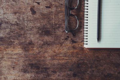 Directly above shot of book with pencils and eyeglasses on wooden table