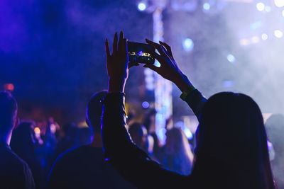 Rear view of woman photographing with smart phone at music concert