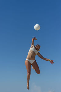 Low angle view of person jumping against clear blue sky