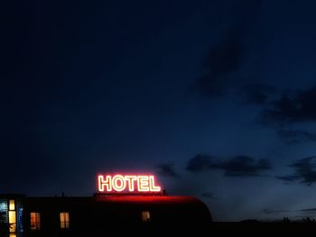 Low angle view of illuminated sign against sky at night